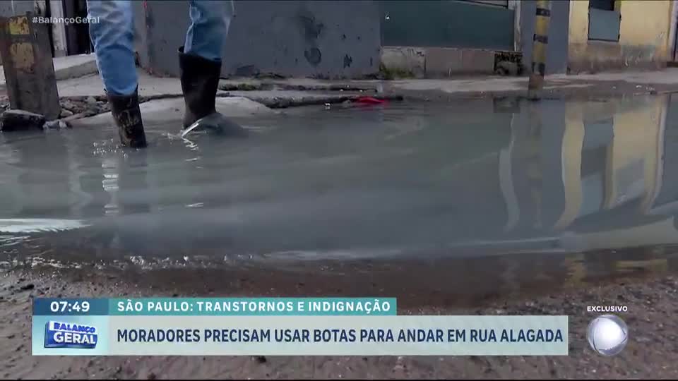 Moradores precisam usar botas para andar em rua alagada na zona leste de São Paulo